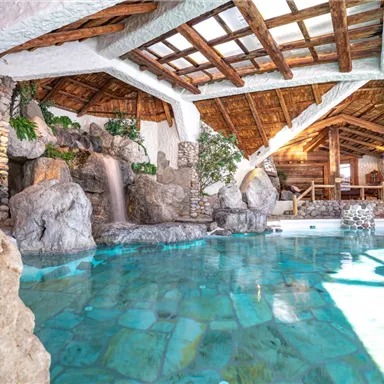 A beautiful indoor pool with clear, greenish water and a rustic wooden structure. Rock formations and plants create a relaxing atmosphere.