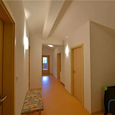 A bright hallway with several doors and a colorful seating area. The walls are white and the lighting creates an inviting atmosphere.
