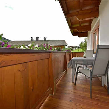 A cozy balcony with a wooden fence and blooming plants. There is a table and a chair, perfect for relaxing hours outdoors.