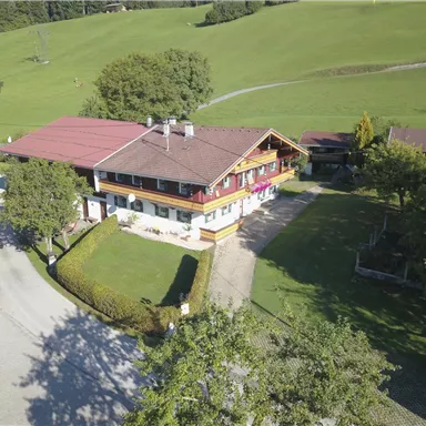 A picturesque house with a red roof, surrounded by green meadows and trees. The surroundings are calm and inviting.