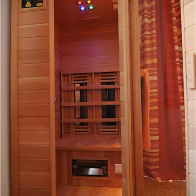 A sauna with wooden paneling and colorful lights. It is located in a room with a curtain and a mirror.