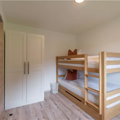 Ein einfaches Zimmer mit einem Etagenbett und einem Schrank. Der Raum ist hell und freundlich gestaltet.