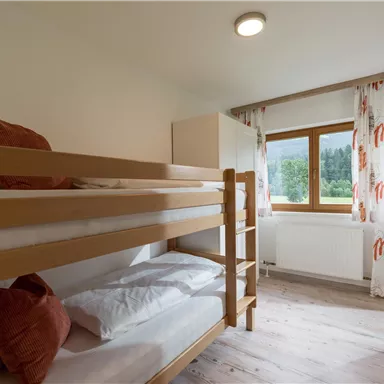 Ein einfaches Schlafzimmer mit einem Etagenbett und einem Fenster, das einen Blick auf die Natur bietet. Die Fenster sind mit Vorhängen geschmückt, und der Raum hat einen hellen, einladenden Eindruck.