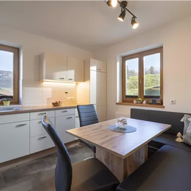 Eine moderne Küche mit Fenster und einem gemütlichen Essbereich. Die Möbel sind in hellen Farben gehalten und es gibt eine schöne Aussicht auf die umliegende Landschaft.