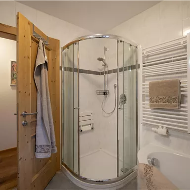 Ein modernes Badezimmer mit einer Duschkabine aus Glas und einem Holzschrank. Die Wände sind hell gefliest und ein Handtuchhalter ist vorhanden.