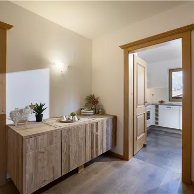 Ein heller Flur mit einem modernen Holzschrank und einer Pflanzenarrangement. Im Hintergrund ist eine offene Tür zur Küche sichtbar.