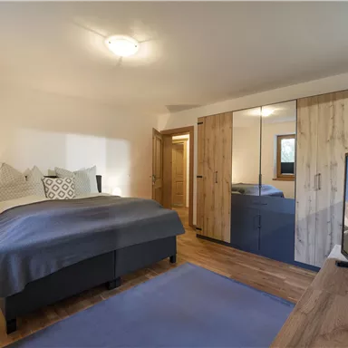 Ein modernes Schlafzimmer mit einem großen Bett und Holzmöbeln. Der Raum ist hell und einladend, mit einem Fernseher und einem großen Kleiderschrank.