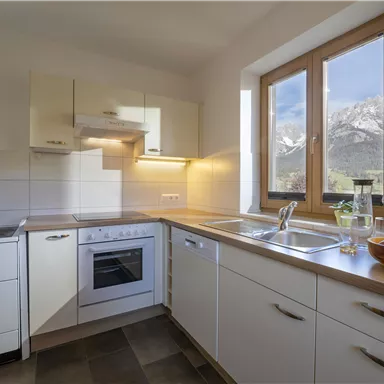 Eine helle und moderne Küche mit Fenster, das einen Blick auf Berge bietet. Schlichte Möbel und eine einladende Atmosphäre.