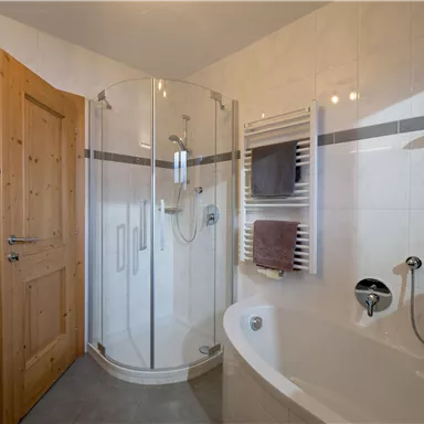 Ein modernes Badezimmer mit einer Duschkabine und einer Badewanne. Die Wände sind hell gefliest und es gibt einen Handtuchwärmer.