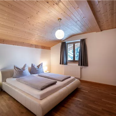 Ein gemütliches Schlafzimmer mit zwei Betten und einem Holzdecke. Das Zimmer ist hell und modern eingerichtet, mit Fenstern und einer Lampe.