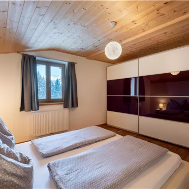Ein modernes Schlafzimmer mit einem Holzdecke und einem großen Fenster. Die Betten sind mit hellen Kissen und Decken ausgestattet, und ein geräumiger Kleiderschrank ist im Raum.