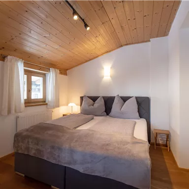 Ein gemütliches Schlafzimmer mit einem Doppelbett und hellem Holzdecke. Die Fenster lassen viel Licht herein und sorgen für eine entspannte Atmosphäre.