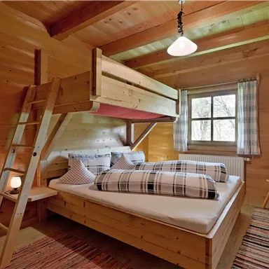 Ein gemütliches Schlafzimmer aus Holz mit einem Etagenbett und einem großen Fenster. Der Raum ist hell und freundlich eingerichtet, ideal für entspannende Nächte.