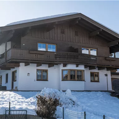 A charming wooden house in alpine style, surrounded by snow. The mountains are visible in the background, and the sky is clear.