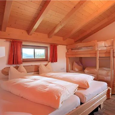 Ein gemütlicher Schlafraum mit zwei Einzelbetten und einem Hochbett. Das Zimmer hat Holzwände und große Fenster mit Aussicht.