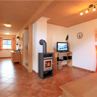 Ein gemütlicher Wohnraum mit einem Holzofen und einem Fernseher. Die Wände sind hell, und es gibt ansprechende Dekorationen und Beleuchtung.