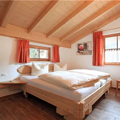 Ein gemütliches Schlafzimmer mit Holzbalken und roten Vorhängen. Es gibt ein großes Doppelbett und einen Stuhl in der Ecke.