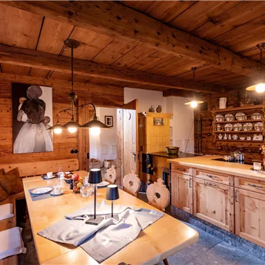 Eine gemütliche Holzhausküche mit einem großen Esstisch und einem rustikalen Thekenbereich. Die Wände sind mit Holzvertäfelungen und Küchenutensilien dekoriert.