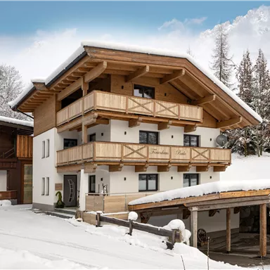 Ein modernes chalet im Schnee, umgeben von verschneiten Bäumen. Das Gebäude hat mehrere Balkone und eine gemütliche Atmosphäre.
