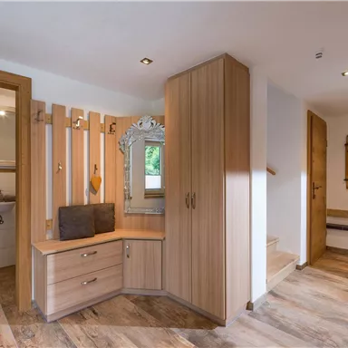 Ein heller Eingangsbereich mit Holzverkleidung und modernem Design. Im Raum befinden sich ein Spiegel und eine gemütliche Sitzgelegenheit.