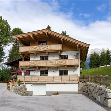 Ein modernes Holzhaus in den Alpen mit mehreren Balkonen. Die Umgebung ist grün und landschaftlich reizvoll, ideal für einen ruhigen Rückzugsort.