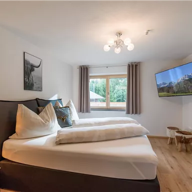 Ein modernes Schlafzimmer mit zwei Betten und großen Kissen. Ein Fernseher und ein Fenster mit Blick auf die Natur sorgen für eine angenehme Atmosphäre.