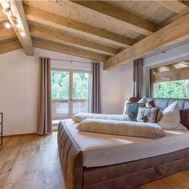 Ein modern eingerichtetes Schlafzimmer mit Holzdecken und einem großen Bett. Die Fenster bieten einen Blick auf die Natur draußen.