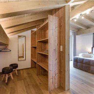 Ein moderner Raum mit Holzregalen und einem kleinen Spiegel. Im Hintergrund ist ein gemütliches Schlafzimmer sichtbar.