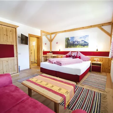 A cozy room with a large bed and a red sofa. Wooden furniture and colorful rugs give the space an inviting atmosphere.