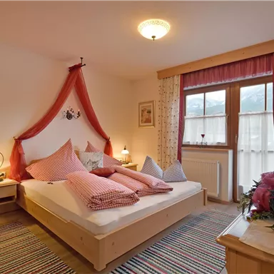 A cozy bedroom with a double bed, decorated with red and white cushions. Large windows provide plenty of daylight and an inviting atmosphere.