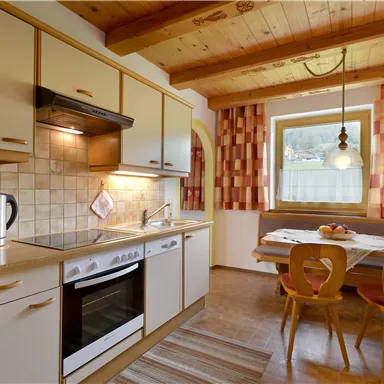 Eine moderne Küche mit hellen Schränken und einem Esstisch. Das Zimmer hat ein gemütliches Ambiente mit Holzdetails und Fenstern mit Blick nach draußen.