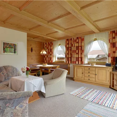 Ein gemütliches Wohn- und Esszimmer mit Holzdecke und farbenfrohen Vorhängen. Es gibt eine gemütliche Couch, einen Tisch und einen Fernseher.