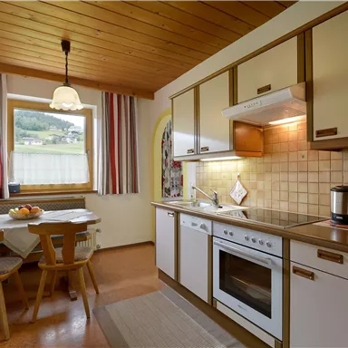 Eine helle Küche mit Holzdecke und modernem Design. Am Tisch stehen frisches Obst und es gibt einen Blick auf die Landschaft draußen.