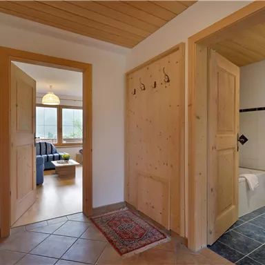 Ein geräumiger Flur mit Holzverkleidung und einem Teppich. Auf der rechten Seite befindet sich ein Badezimmer und im Hintergrund sieht man ein gemütliches Wohnzimmer.