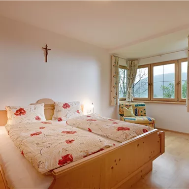 Ein gemütliches Schlafzimmer mit einem Doppelbett und Holzregalen. Das Zimmer hat ein Fenster mit Blick ins Freie und sanftes Licht.