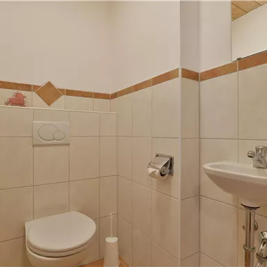 Ein kleines Badezimmer mit einer Toilette und einem Waschbecken. Die Wände sind gefliest in hellen Farben mit dekorativen Fliesen.