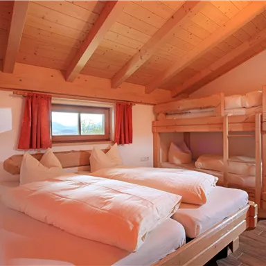 Ein gemütliches Zimmer mit einem Doppelbett und einem Etagenbett. Das Holzdesign und die großen Fenster schaffen eine einladende Atmosphäre.