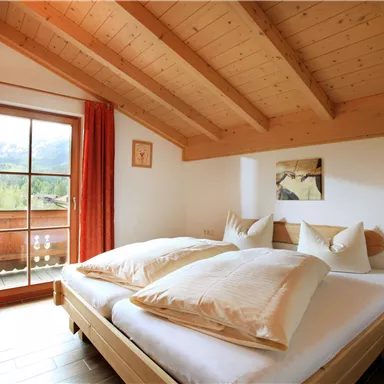 Ein gemütliches Schlafzimmer mit Holzwänden und einem großen Fenster. Es gibt zwei Betten mit großen Kissen und Blick auf die Berge.