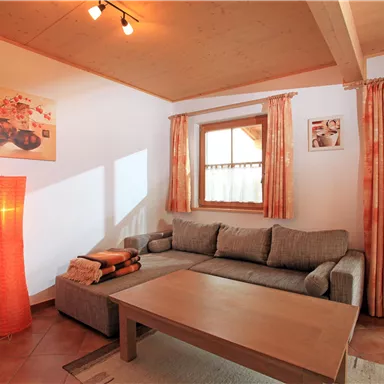 Ein gemütliches Wohnzimmer mit einem grauen Sofa und einem Holztisch. Die warmen Farben der Vorhänge und die Stehlampe schaffen eine einladende Atmosphäre.