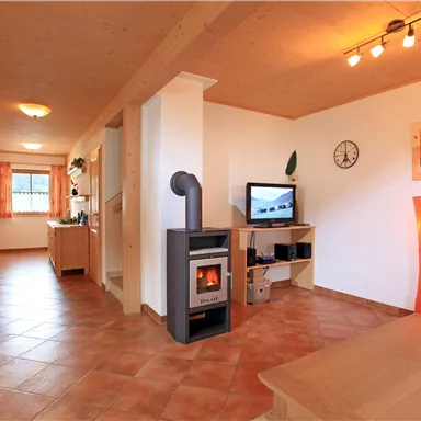 Ein gemütliches Wohnzimmer mit einem Holzofen und einem Fernseher. Die Wände sind hell gestrichen und die Böden sind mit Fliesen ausgelegt.