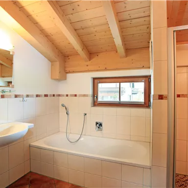 Ein modernes Badezimmer mit Holzbalkendecke. Es gibt eine Badewanne, eine Dusche und ein Waschbecken.