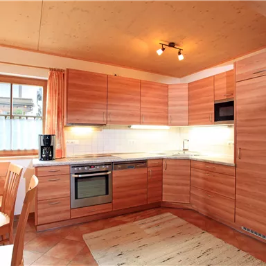 Eine moderne Küche mit Holzschränken und einem großen Fenster. Es gibt einen Tisch mit Stühlen und Kaffeezubereiter.