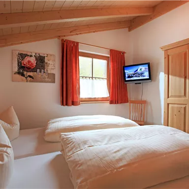 Ein gemütliches Schlafzimmer mit zwei Betten, Holzdecken und einem großen Fenster. Es gibt einen Fernseher und eine Holzkommode im Raum.