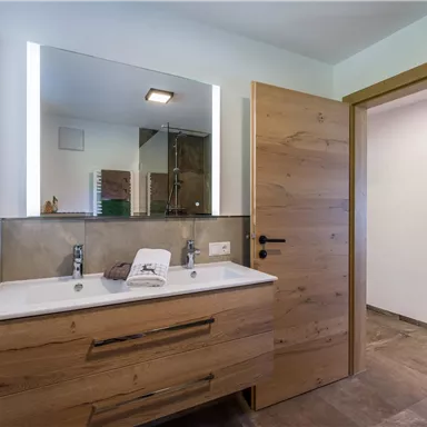 Ein modernes Badezimmer mit einem Holzwaschbecken und einem großen Spiegel. Es gibt eine Glasdusche und eine helle, freundliche Atmosphäre.