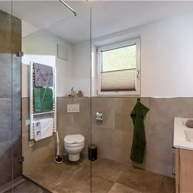 Ein modernes Badezimmer mit gläserner Dusche und eleganten Fliesen. Es enthält ein Waschbecken und Handtücher in neutralen Farbtönen.