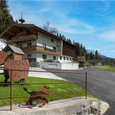 Ein rustikales Gebäude inmitten von Wald, umgeben von einer grünen Wiese. Vor dem Haus stehen dekorative Metallfiguren von Tieren.