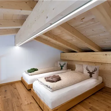 Ein gemütliches Schlafzimmer mit zwei Einzelbetten aus Holz. Die Wände und der Boden bestehen aus hellem Holz, und es gibt dekorative Kissen mit einem Hirschmotiv.