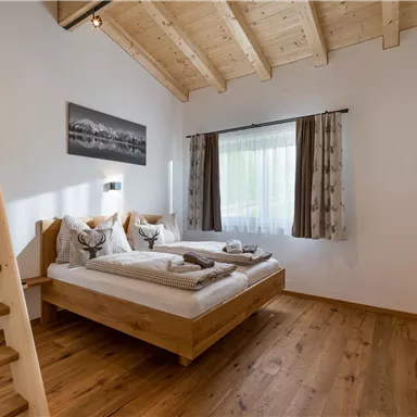 Ein gemütliches Schlafzimmer mit einem Doppelbett und Holzregal. Große Fenster sorgen für viel Licht und eine angenehme Atmosphäre.