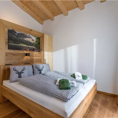 Ein gemütliches Schlafzimmer mit Holzdekor und zwei Betten. Die Dekoration umfasst Kissen mit einem Hirschmotiv und grüne Handtücher.