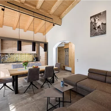 Ein modernes, helles Wohnzimmer mit offenem Küchenbereich. Holzdetails und eine einladende Atmosphäre sorgen für Gemütlichkeit.